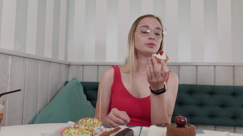 Beautiful young girl sits at a table in a cafe and eats sweet fresh desserts from a plate.