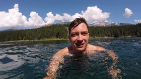 4k selfie video of a young man swimming. Selfie stick video of young person swimming in a lake on a sunny day in switzerland at caumasee. Point of view POV video of young man swimming