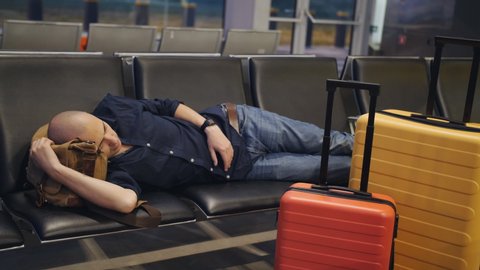Man sleeping through the night at the airport due to flight delays. Tired man sleeping on the seats in the waiting room of the airport.