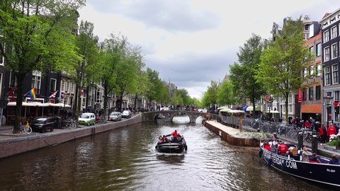 Holland, Amsterdam - 02/05/2019 EDITORIAL: Touristic boats floating Amsterdam canal on a cloudy day. eople walking and riding bicycles. Beauty of old european city centre.