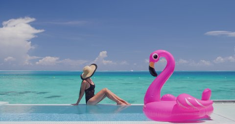 Travel Vacation Woman in bikini and inflatable pink flamingo float pool toy mattress in swimming pool. Girl sunbathing enjoying holidays at resort pool living luxury lifestyle.