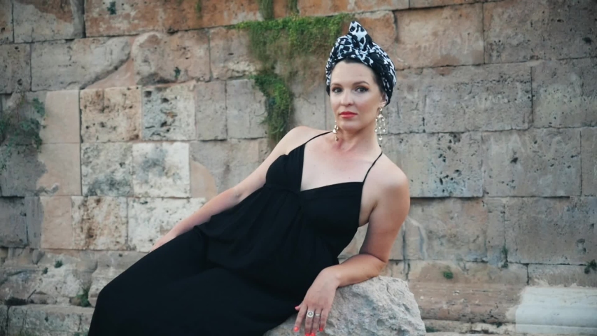 Beautiful young attractive Muslim woman in long black dress and headscarf (turban) standing on the corner of Hidirlik tower old Roman Empire tower in Antalya, Turkey