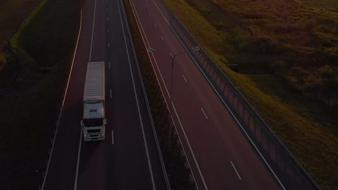 Large Delivery Truck is Moving Setting Sun. Aerial Shot Of Truck On Road In Beautiful Countryside in Sunset. Aerial View of Semi-truck on Road With Sunset In Background. 