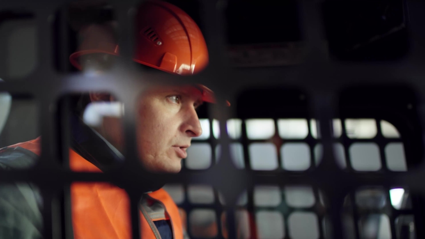 operator man in a helmet and overalls sitting in new loader and studing it