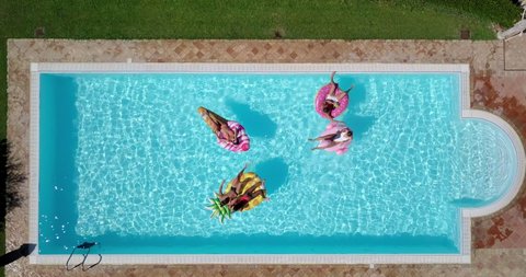 Aerial shot of young multi-ethnic friends in swimwear are relaxing in swimming pool with colorful inflatables in a sunny day.