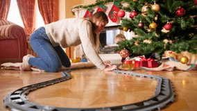 4k video of happy smiling family with little boy building railroad for small toy train around Christmas tree. Child receiving gifts and presents from Santa Claus on winter holidays and celebrations