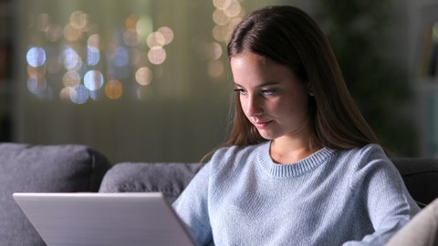 Excited woman checking laptop celebrating good news sitting on a couch in the living room at home in the night