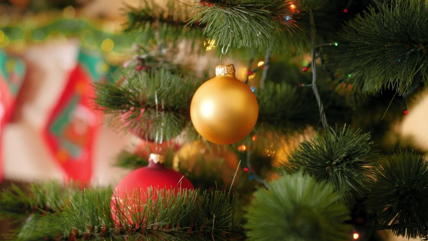 Closeup 4k footage of golden bauble hanging on Christmas tree branch against blinking and glowing Christmas lights garland on branch | Shutterstock HD Video #1037775368