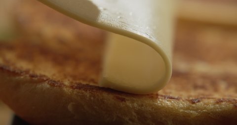 Macro shot of piece of cheese placed on bun for fried crust for burger. 4K Slow Motion