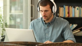 Excited man wearing headphones reading content on laptop finding offers sitting in a coffee shop