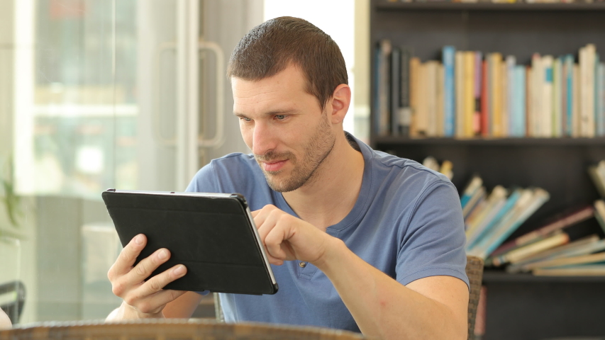Happy man using a tablet to watch on line media sitting in a coffee shop