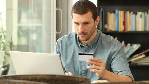 Worried man buying online with credit card and laptop in a coffee shop
