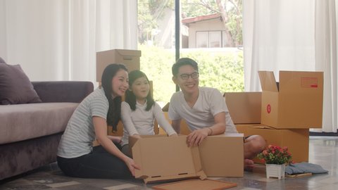 Happy Asian young family relocation removals settle in new home. Chinese parents and kids open cardboard box or parcel unpacking in living room on moving day. Real estate dwelling, loan and mortgage.