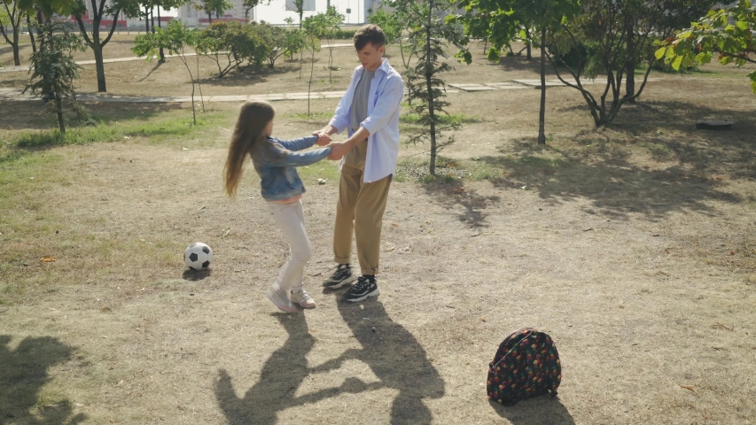Teenage brother circling his smaller happy sister around having fun together in park at sunny weekend day