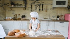 Happy baby girl in the kitchen playing with flour to have fun. A child dressed as a cook. 4K video.