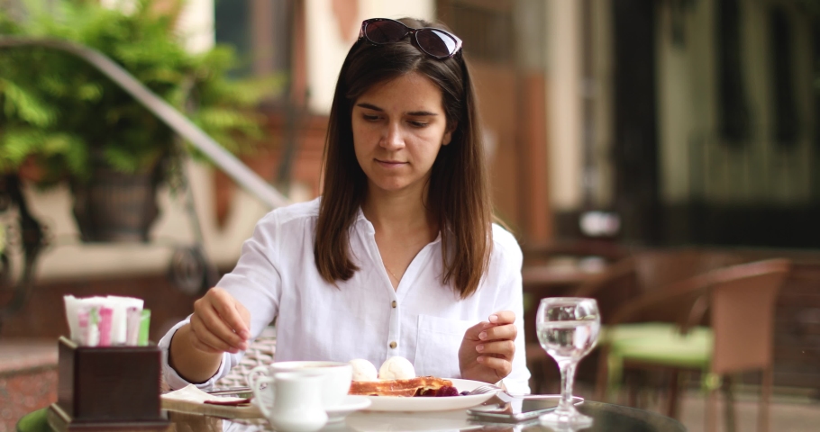 Beautiful young woman drinking coffee and eating delicious waffles at table in outdoor cafe