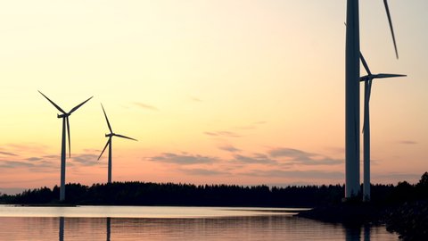 Four wind turbines, part of island based wind farm, spin at sunset. Silhouettes long shot at real wind speed, in Finland near Baltic sea shore.