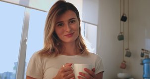 Portrait of the young beautiful Caucasian woman smiling happily to the camera in the kitchen in the morning with a cup of tea or coffee. Close up.