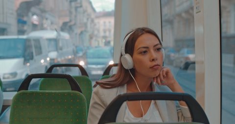 Young beautiful Caucasian woman in big white headphones sitting in the empty tram and listening to the music while going home or to work.