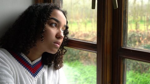 Sad depressed beautiful mixed race African American girl teenager young woman sitting looking out of a window 