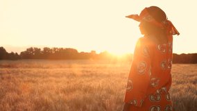 HD Video clip of African woman farmer in traditional clothes standing in a field of crops, wheat or barley, in Africa at sunset or sunrise looking at the sun