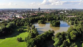 Fly over Kleinhesseloher Lake and Englischer Garten, a large public park in the centre of Munich, Germany. City skyline, drone video