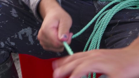 A daylight extreme closeup shot of a boats deck crew tying knots one by one on each end of the green nylon rope by hand..