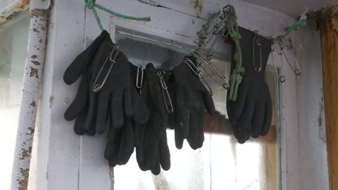 A daylight closeup shot of several black rubber gloves along with large safety pins hanging by the window in the wall of a boat.
