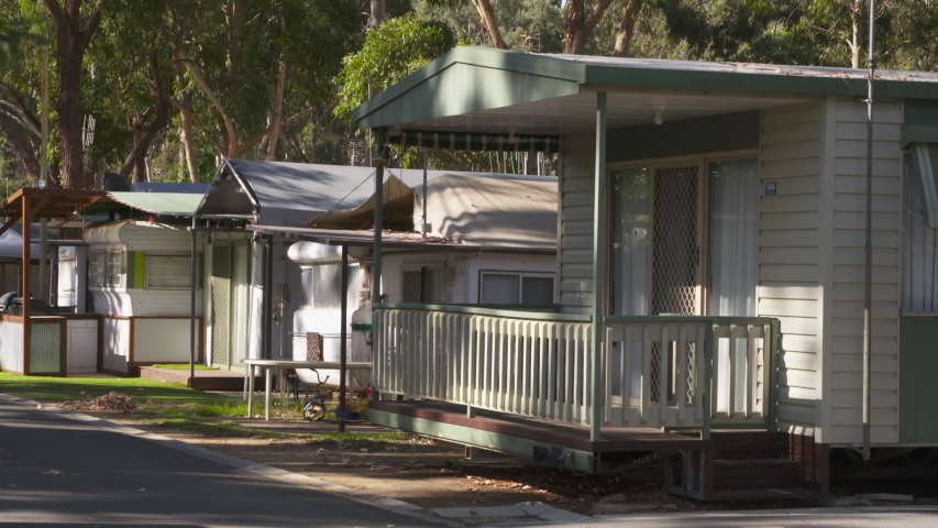 A still focused shot of thin green leaves swaying from side to side with blurred caravans in the background. 