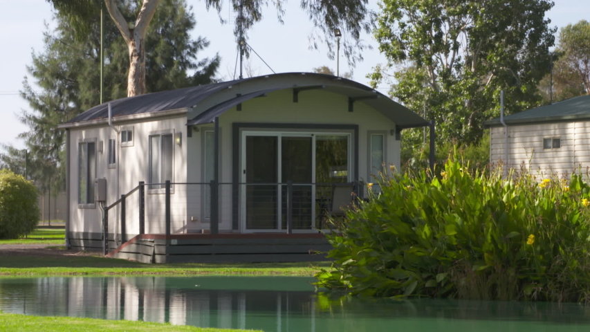 A still long shot of a standing caravan at a caravan park, shifting into a pan towards the other caravans