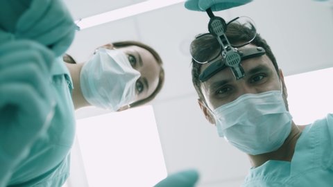 At the dentist. Handsome young dentist in surgical mask is holding tools and looking at camera. Surgeons are standing above of the patient before surgery Stock Video