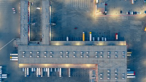 Aerial top view of the large logistics park with warehouse, loading hub with many semi-trailers trucks standing at the ramps for load/unload goods at night. Hyper lapse (hyperlapse - time lapse)