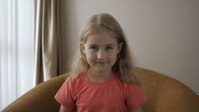 Happy Cute Little Vlogger Saying Hello Hi Looking At Camera Talking To Webcam. Kid Child Girl Making Online Video Call Recording Vlog Sitting On Sofa , Portrait. Funny Girl Smiling Looking At Camera. 