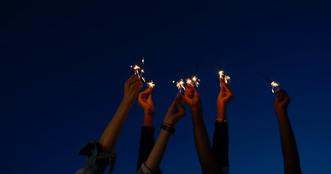 close up of hands of girls holding sparklers . Group of friends celebrating waving sparkler fireworks dancing enjoying party having fun holiday celebration at evening social gathering on rooftop 4k