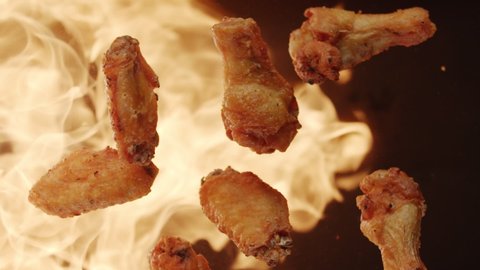 Top view of fried chicken wings flying upwards with blazing fire. Slow motion video on black background
