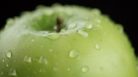 in the video we see a green apple, in the middle of the video the water begins to pour from the top like a shower, black background, close-up