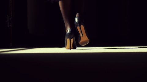 Following Shot of Silhouette of Female Legs in High Heels Shoes Walking Along Dark Hallway. Black and White Slow Motion. Beautiful Scene of Woman Walking Gracefully.