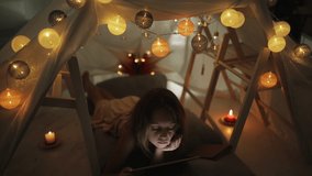 Little 10 year old girl using tablet under her home-made tent inside the living room.