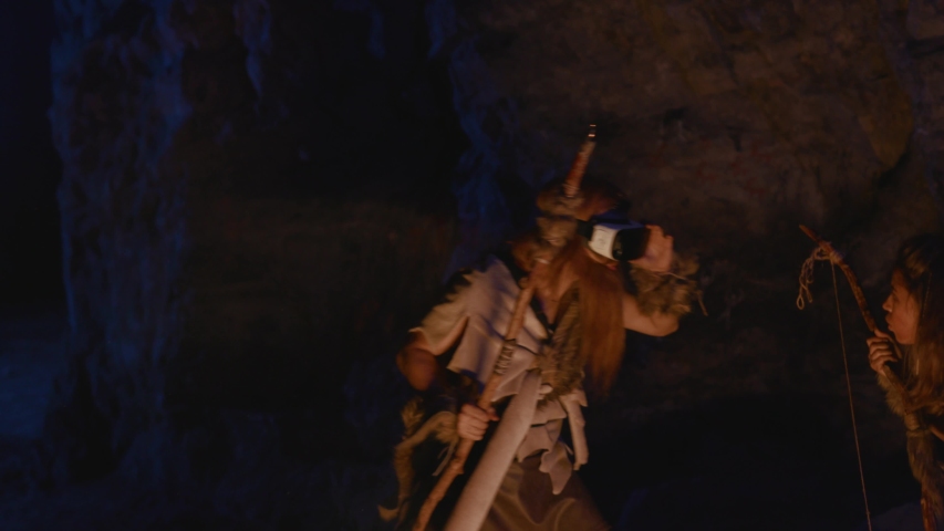 Ancient savage human tribe using modern VR headset technology device staying in cave dwelling at night. Wildlife. Evolution concept.