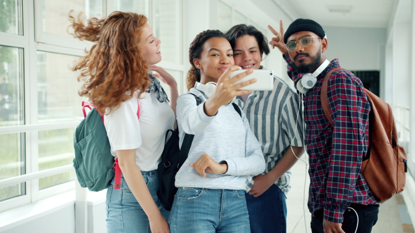 Multi-ethnic group of students girls and guys is taking selfie with smartphone in high school showing hand gestures thumbs-up having fun together. Royalty-Free Stock Footage #1037842595