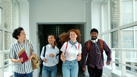 Happy friends girls and guys are running in school hallway doing high-five laughing jumping holding books. People, lifestyle and positive emotions concept.