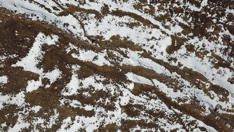 A quick descent down the drone. View of snow, relief land, yellow grass and stones. Feelings of falling and twisting. Mountainous area. Almaty, Kazakhstan.