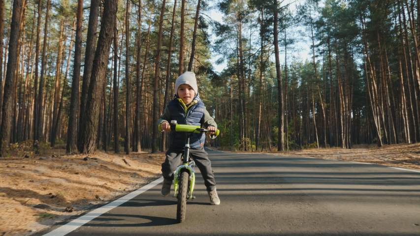 Little boy 4 years old rides a balance bike on a pedestrian road through an autumn pine forest. Front view, slow-motion