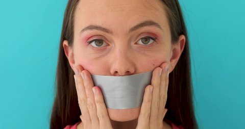 Young woman with her lips covered by a tape over blue background