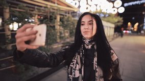 Beautiful young woman make a selfie in a night city photographing herself by smart phone