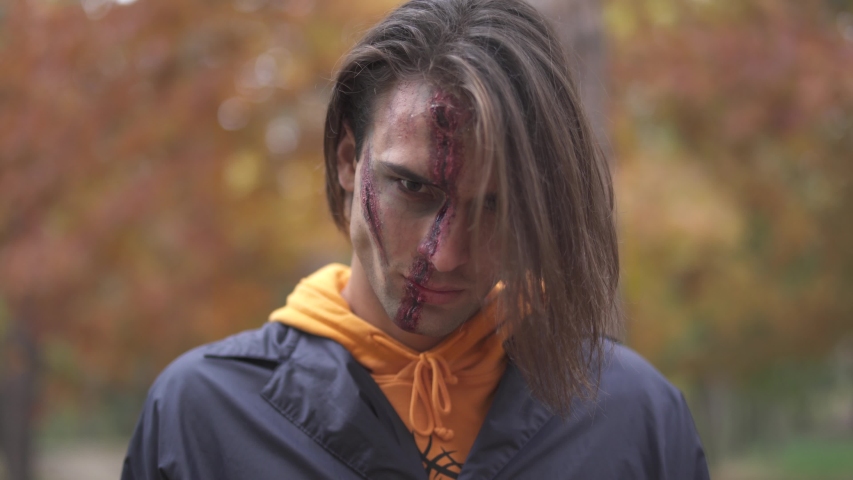 Handsome man with big ugly scar on his face demonstrating two cleavers, rubbing them on each other. The guy with Halloween makeup on face rubbing his knives with an evil look. Focus changing