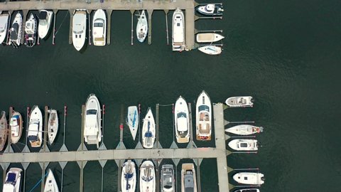 Aerial view of a white motor yacht. Yacht enters the bay in the parking lot. Gdynia, Poland. Many different yachts, catamarans moored to piers. Drone shot 4K.