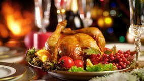 Closeup 4k video of tasty roasted chicken on big plate against burning fireplace and colorful Christmas lights. Dining table served for big family on winter holidays and celebrations.