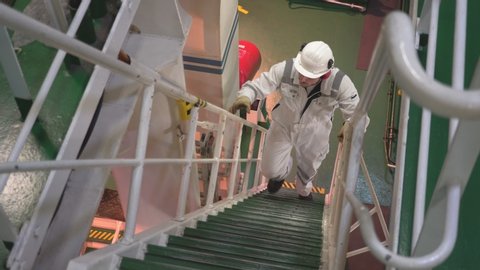 engineer in protective clothing and helmet climbs upstairs in the engine room of the vessel