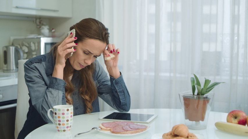 Worried woman having serious conversation during breakfast. Closeup woman arguing on phone in modern kitchen. Anxious girl talking mobile phone at home. | Shutterstock HD Video #1037884736